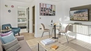 Una sala moderna con sofá, sillas, una mesa de centro y televisor. Hay una zona de comedor con mesa y sillas. La habitación tiene un ventanal grande y obras de arte en las paredes.