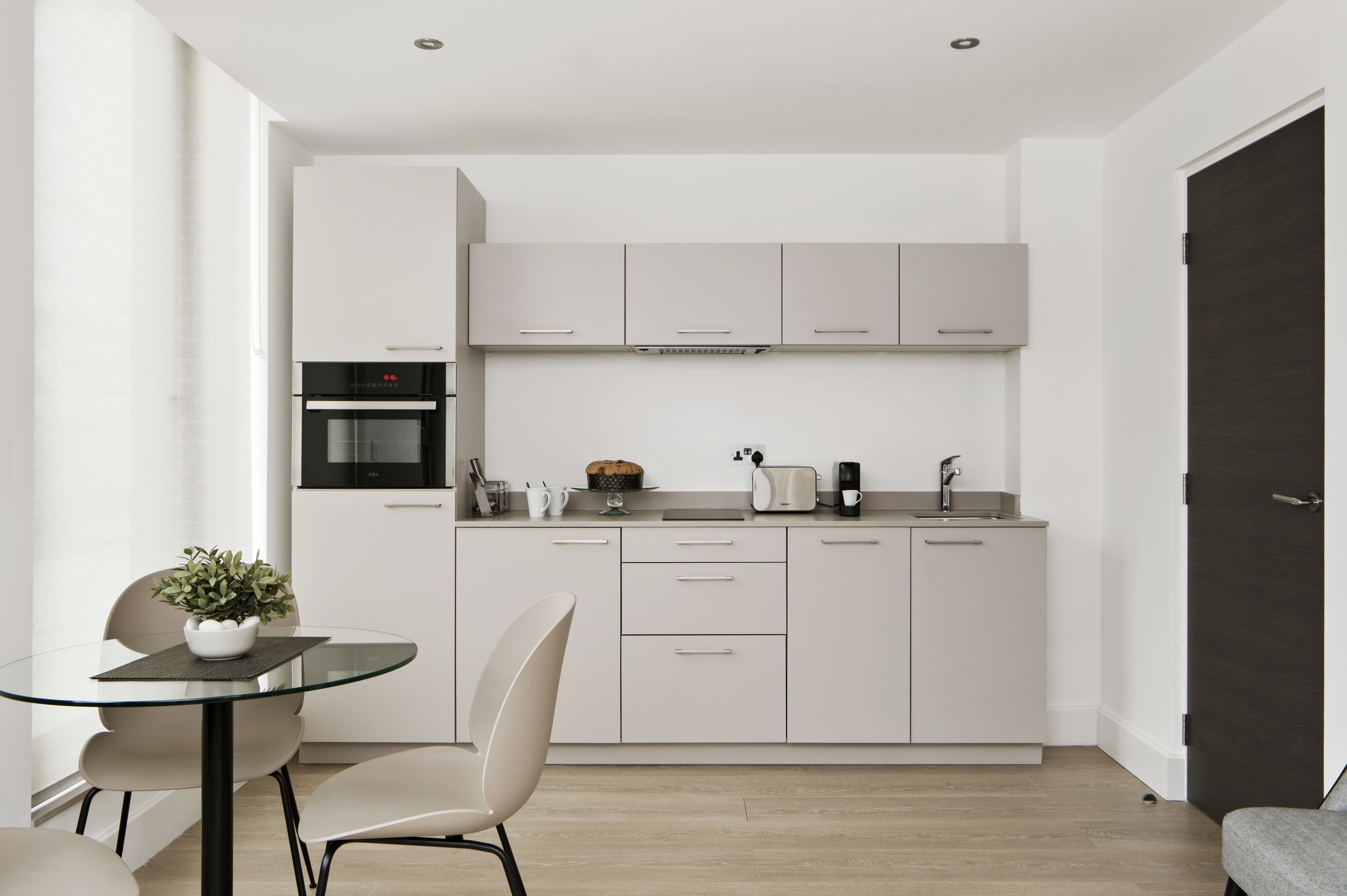 Een moderne keuken met witte kastjes, een inbouwoven en een koffiezetapparaat.