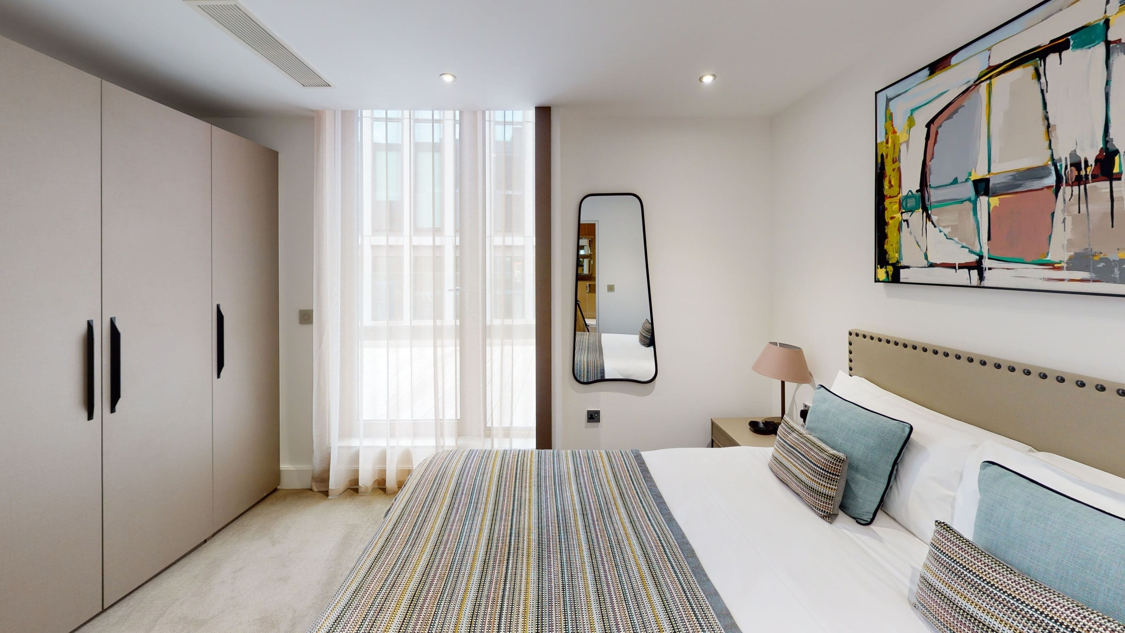 Quarto moderno com cama grande, guarda-roupa, espelho e um quadro na parede.