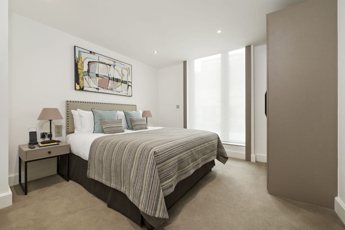 Un dormitorio moderno con una cama grande, una mesita de noche, una lámpara y un cuadro en la pared.