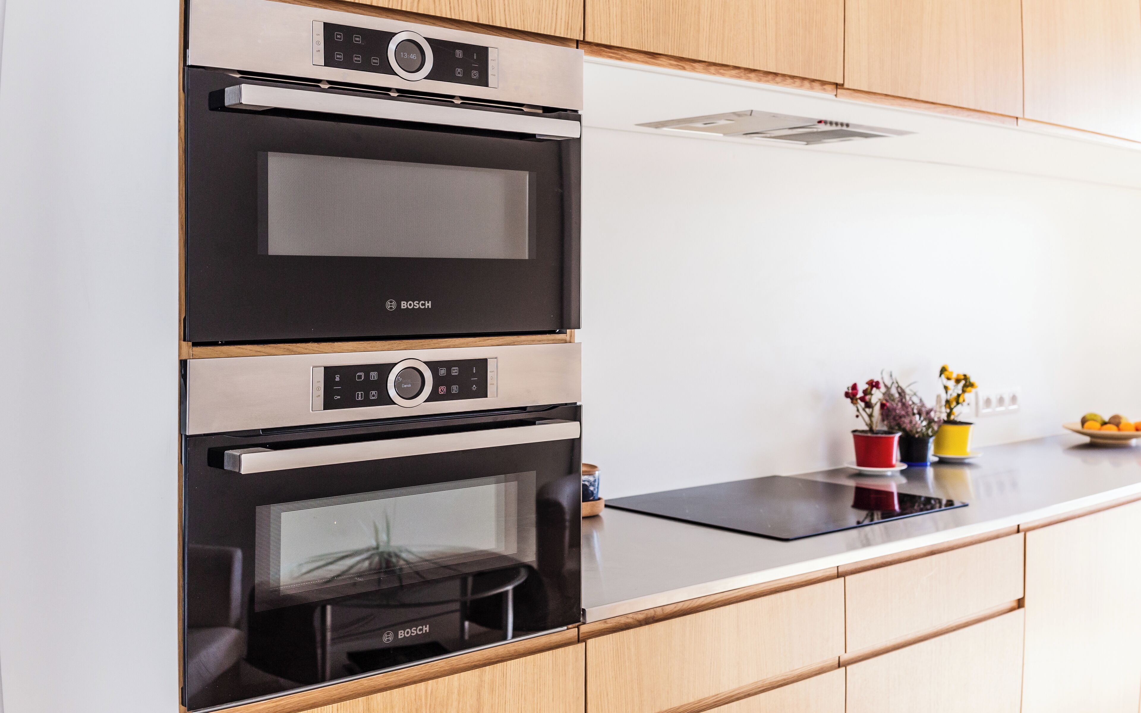 Una cocina con horno y microondas Bosch, armarios de madera y encimera con plantas en macetas.