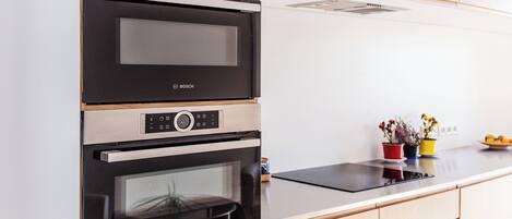 Una cocina con horno y microondas Bosch, armarios de madera y encimera con plantas en macetas.