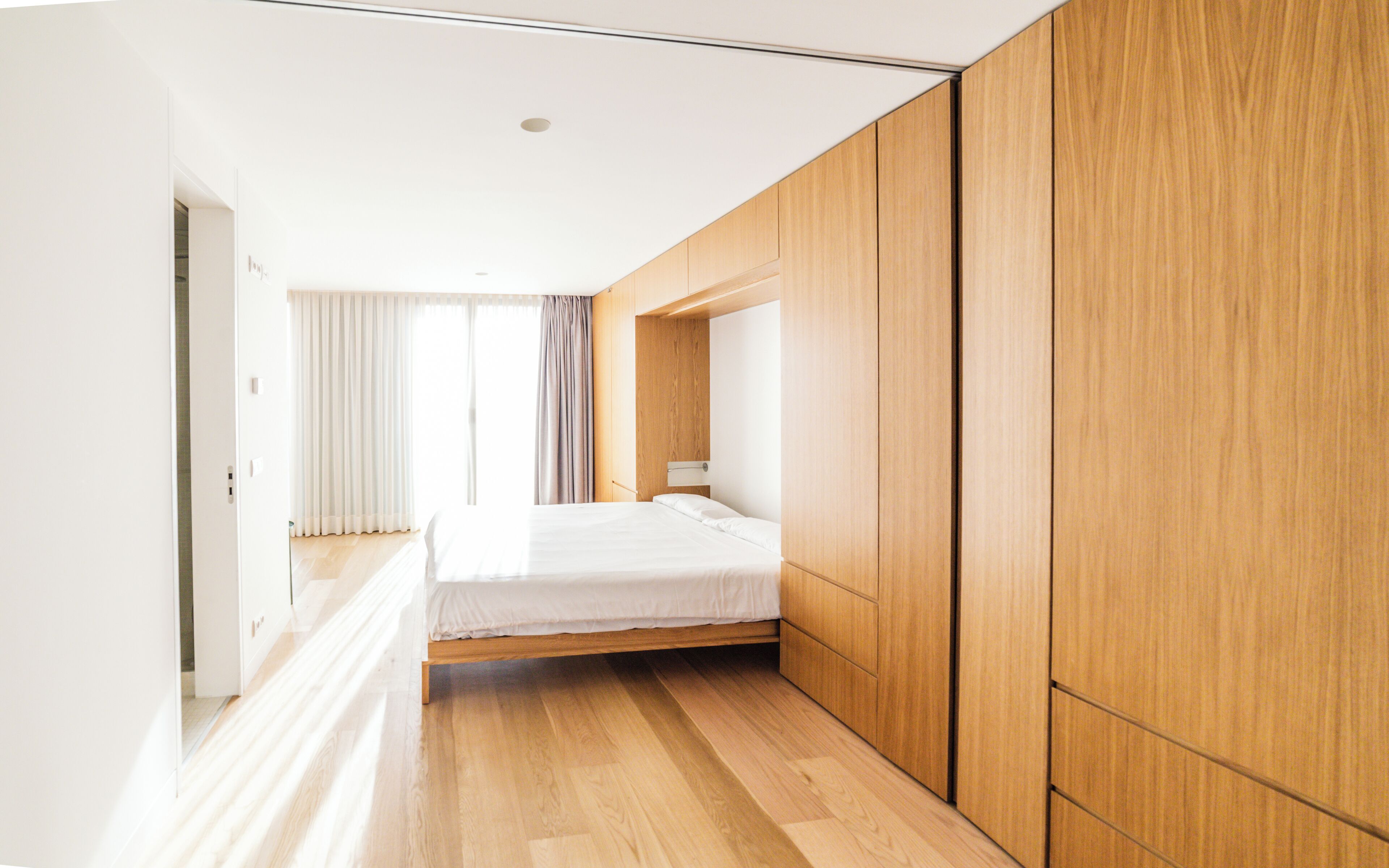 A modern bedroom with a bed, wooden wardrobe, and a view of the outside.