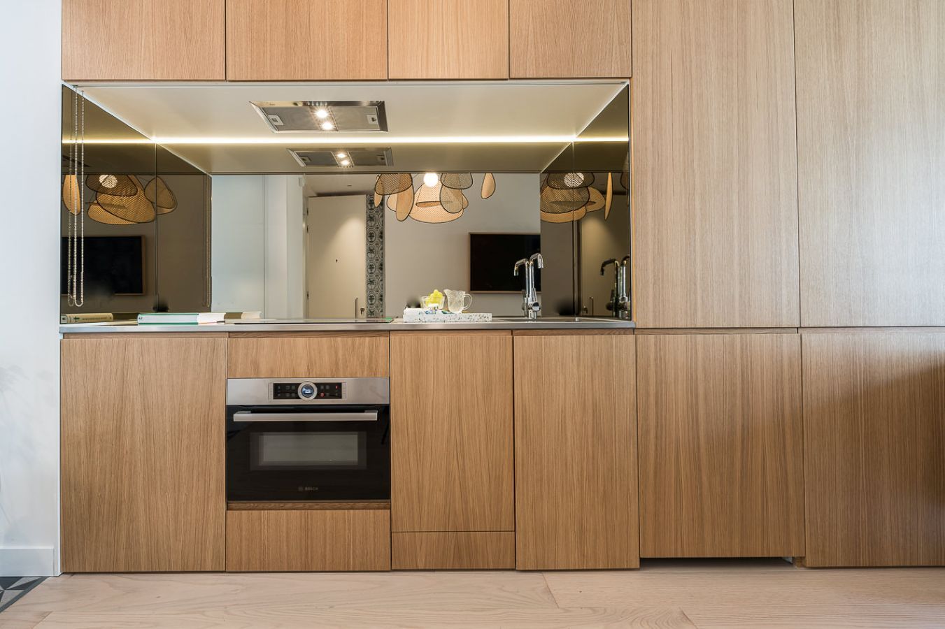 A modern kitchen with wooden cabinetry, a built-in oven, and pendant lighting.