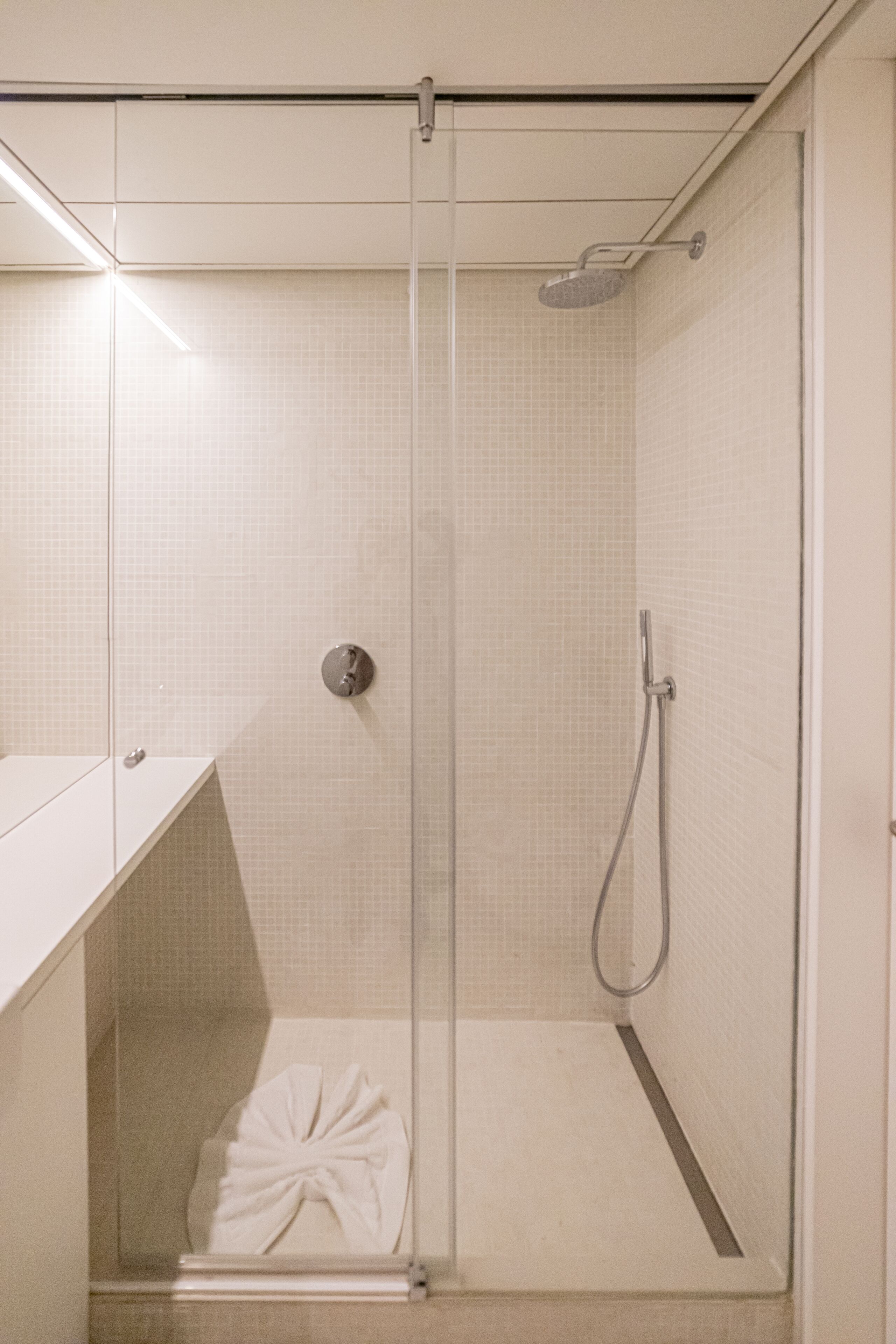 Un baño moderno con ducha envuelta en vidrio, un perchero y un lavabo blanco.