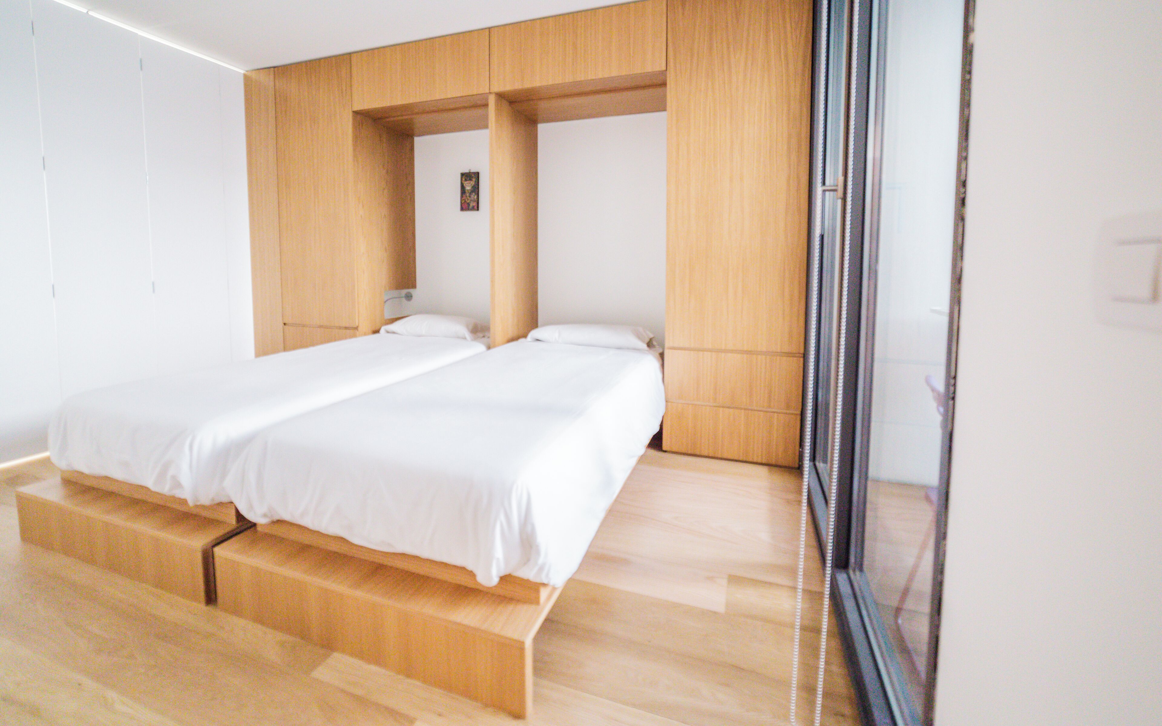 A modern bedroom with a large bed, wooden paneling, and a sliding glass door.