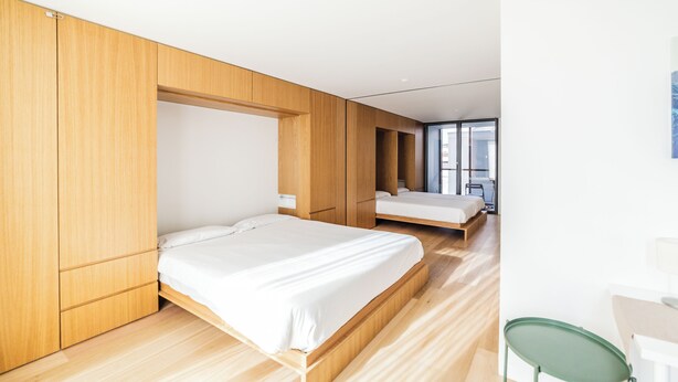 A modern bedroom with two beds, wooden paneling, and a view of the city through large windows. - Edmond Vibes Barrio de Salamanca (Madrid)
