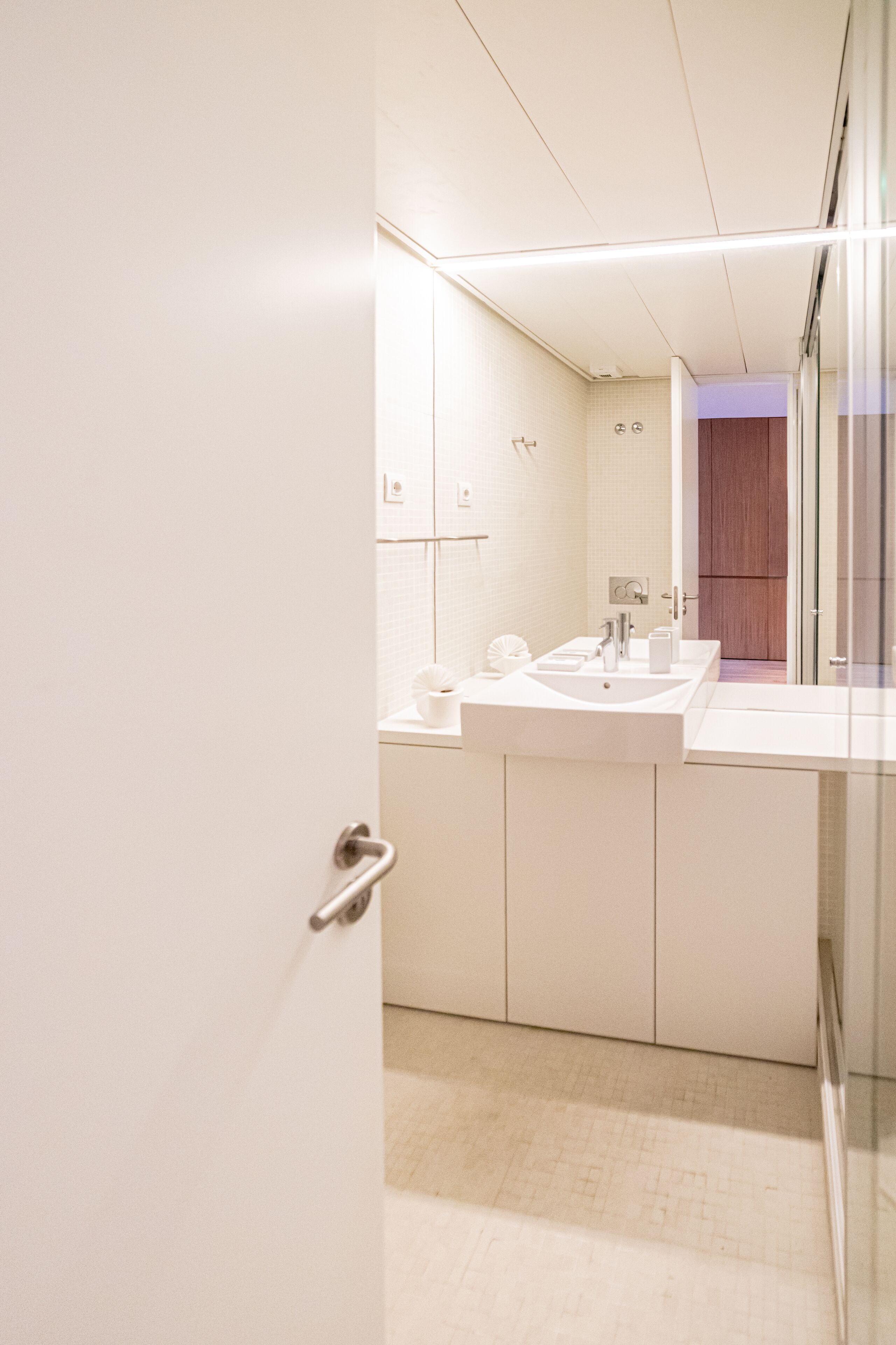 Un baño moderno con lavamanos blanco, espejo y cabina de ducha de vidrio.