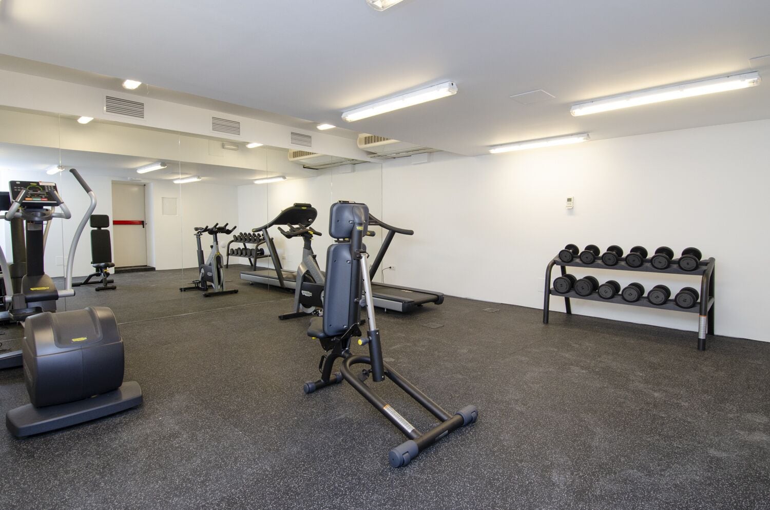 Une salle de sport équipée de tapis de course, d’appareils de musculation et d’une série de haltères.