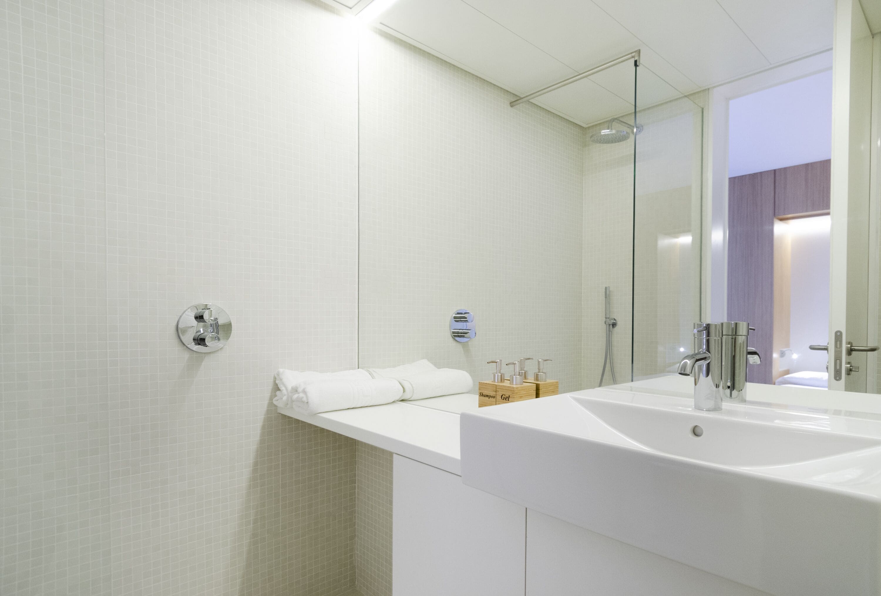 A modern bathroom with a large mirror, white tiles, a sink, and a shower.