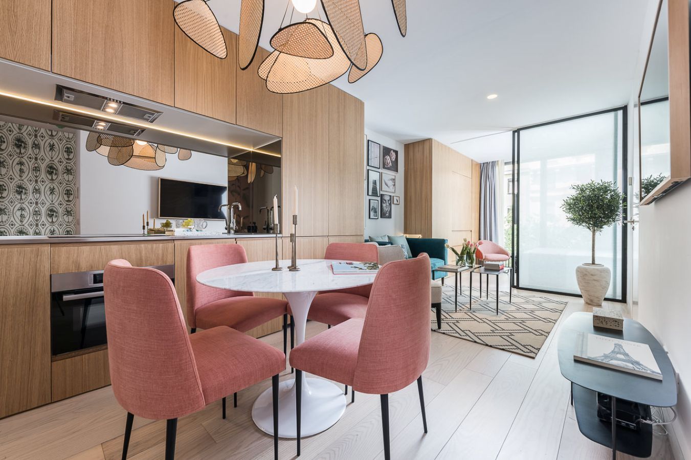 Una cocina moderna con armarios de madera, un comedor con sillas rosa y un ventanal con vistas.
