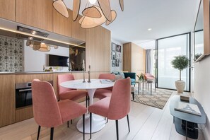 A modern kitchen with wooden cabinets, a dining area with pink chairs, and a large window with a view.
