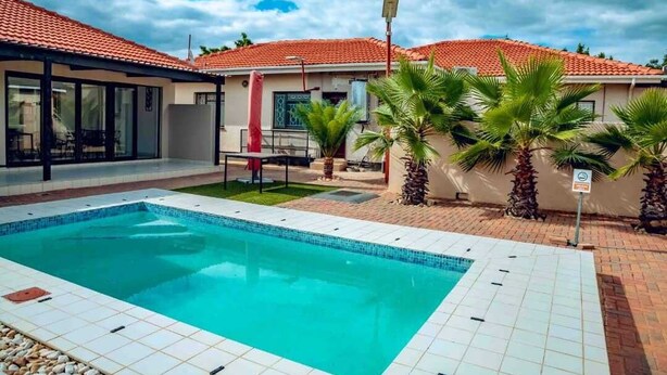 Una piscina con bordes de azulejos, una zona de estar cubierta y palmeras.