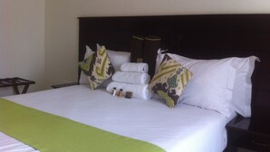 Una cama bien hecha con sábanas blancas, un plaid verde y almohadas decorativas.