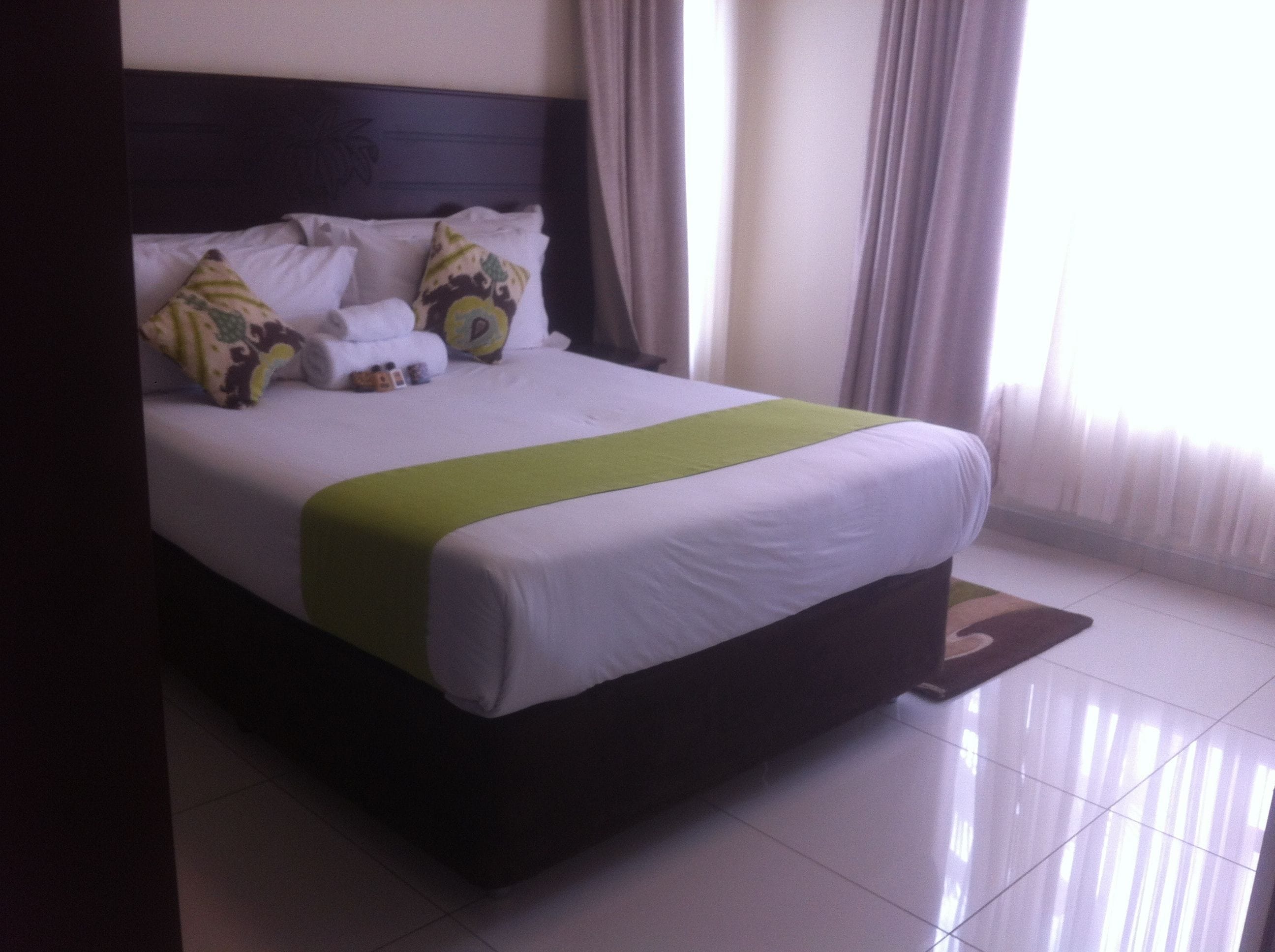 A neatly made bed with white linens, a green throw, and decorative pillows.