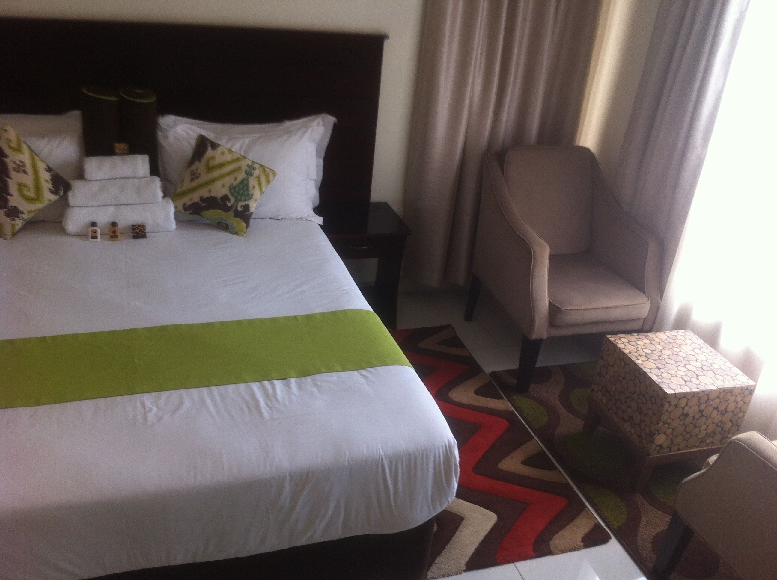 Een hotelkamer met een net opgemaakt bed, een stoel, een klein tafeltje en een nachtkastje.