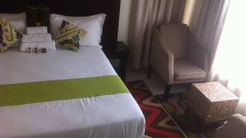 Een hotelkamer met een net opgemaakt bed, een stoel, een klein tafeltje en een nachtkastje.