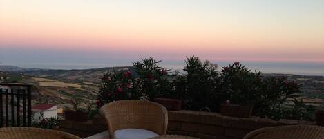 A wicker outdoor seating area with a view of the countryside at sunset.
