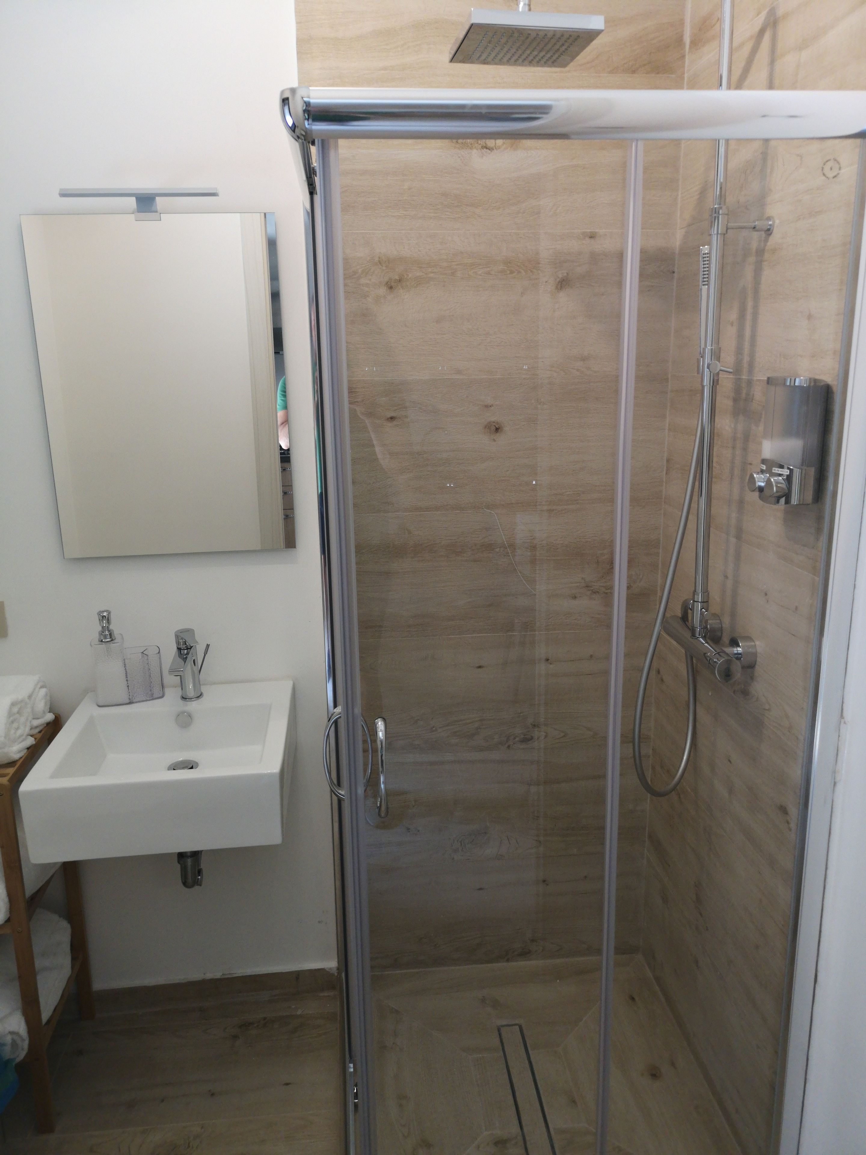A modern bathroom with a glass-enclosed shower, a white sink, and a mirror.