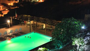 A swimming pool with lounge chairs and tables, surrounded by greenery and a stone wall. - B&B Montemare (Agrigento)