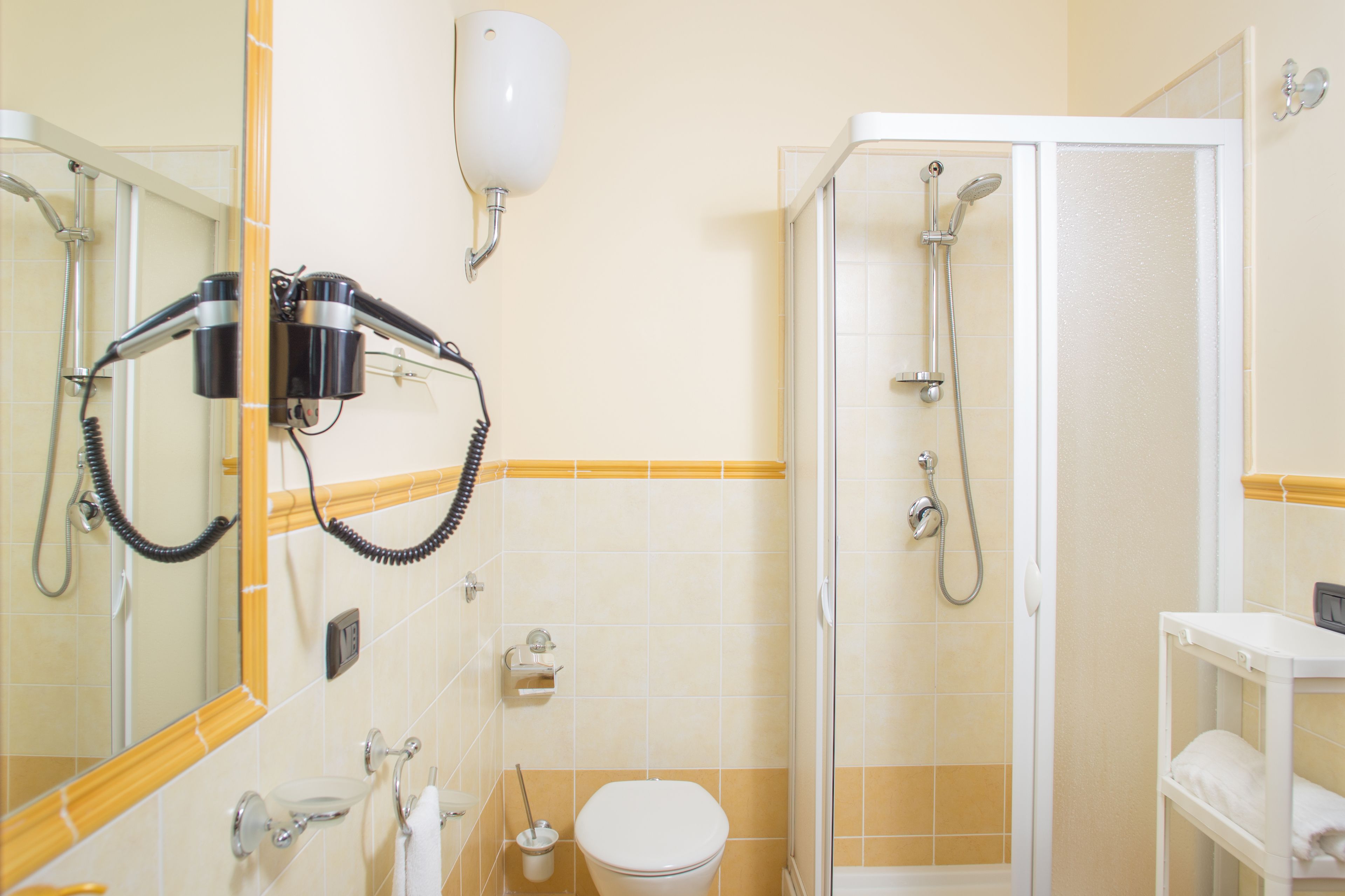 A bathroom with a toilet, a sink, a mirror, a hairdryer, and a shower.