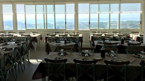 A dining area with multiple tables and chairs, large windows offering a view of the landscape. - B&B Montemare (Agrigento)
