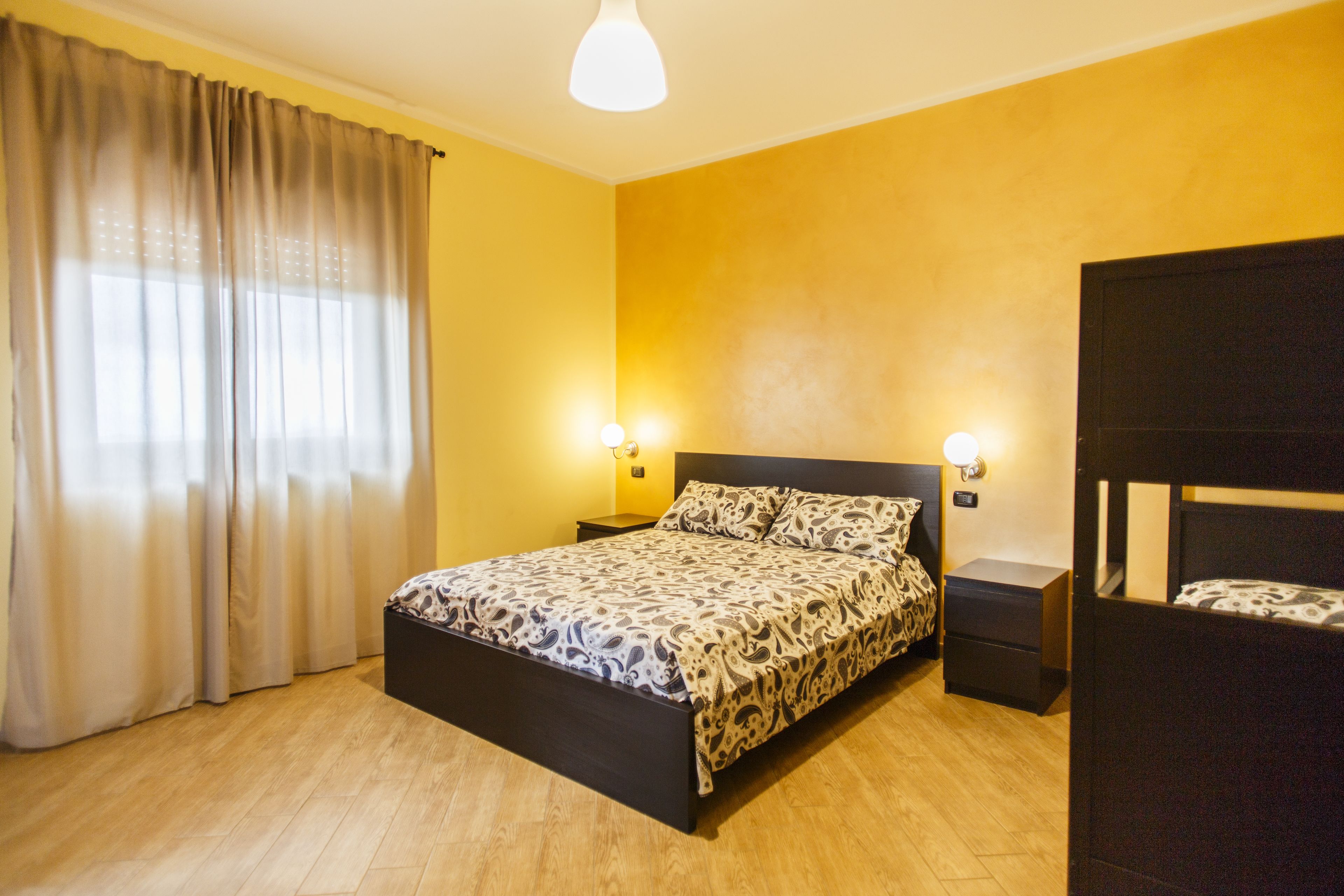 Une chambre à coucher comprenant un lit, des tables de chevet, une armoire et une fenêtre avec des rideaux.