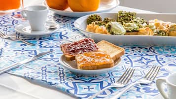 A breakfast setting with toast, jam, and a plate of vegetables on a table with a blue and white patterned tablecloth.