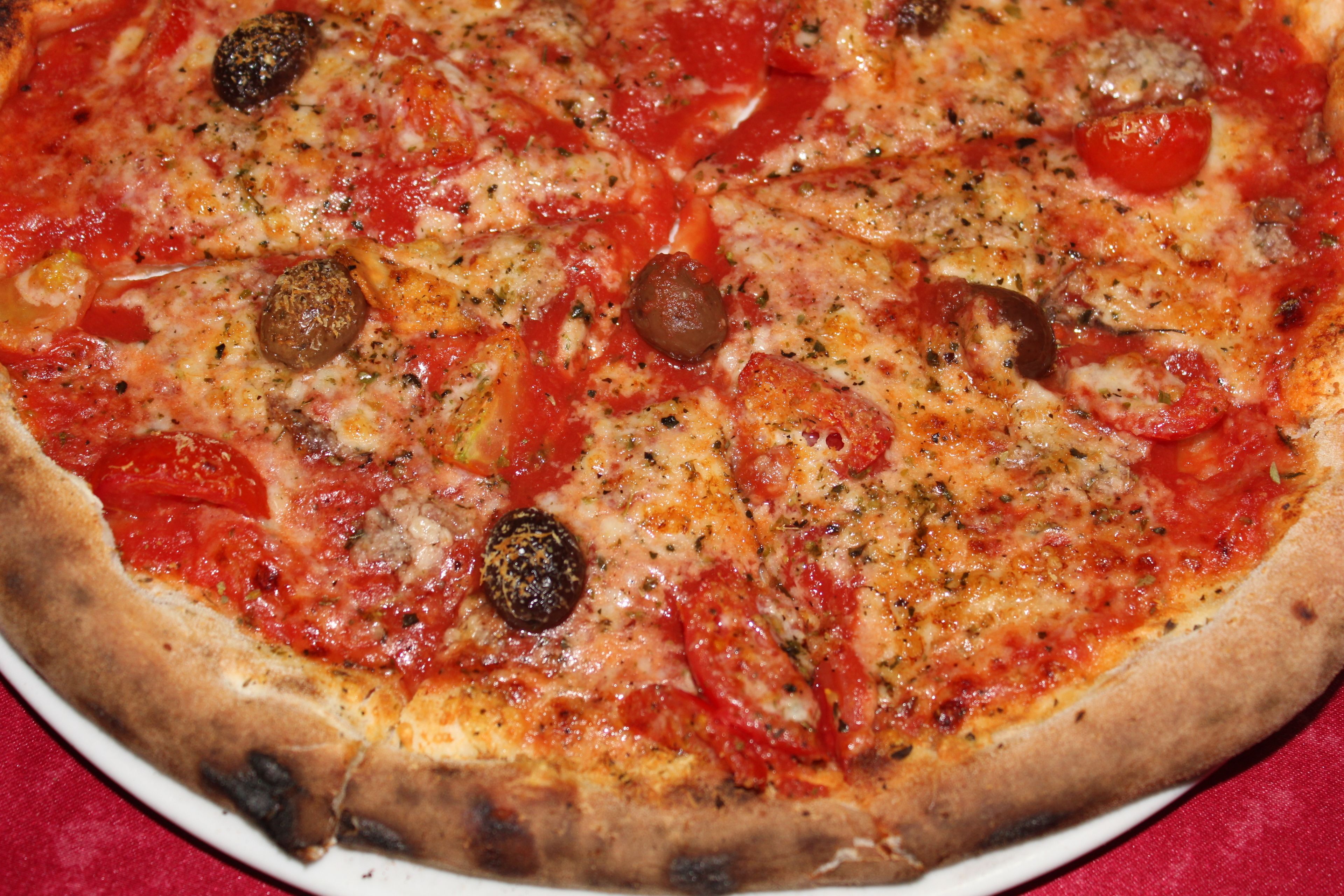 Une pizza garnie de divers ingrédients, notamment des olives, des tomates et des herbes.