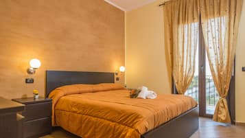 A bedroom with a large bed, two bedside tables with lamps, a window with curtains, and a view of the outdoors.