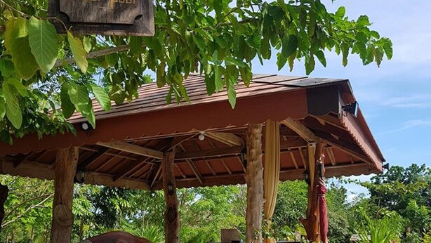 A covered outdoor seating area with wooden tables and chairs, surrounded by potted plants and a sign with a humorous message. - Wonderfarm Villa (Calatagan)