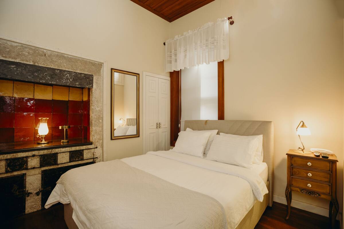 A bedroom with a bed, bedside table, lamp, and a mirror.