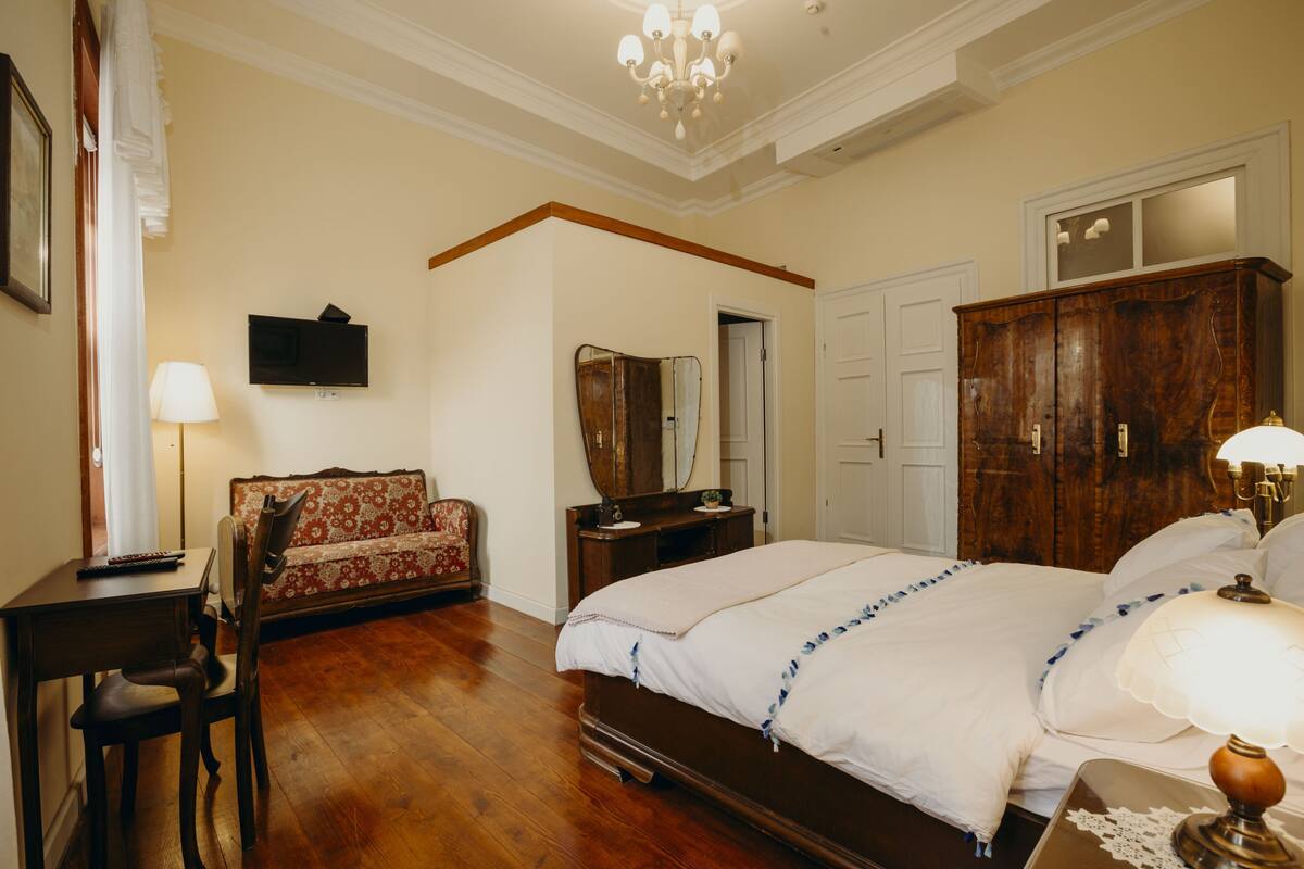 A bedroom with a bed, a desk, a chair, a television, a mirror, and a wardrobe.