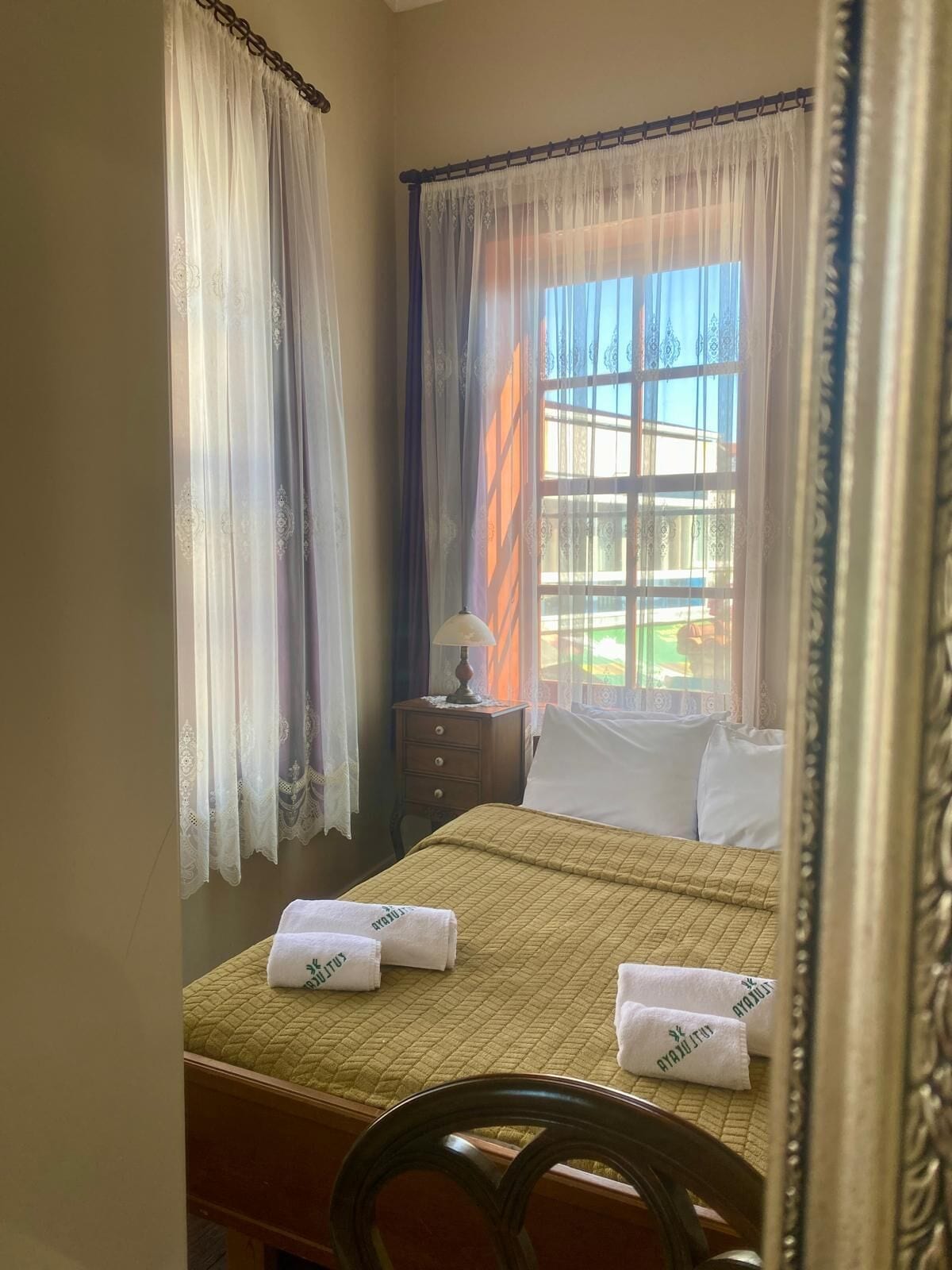 A hotel room with a bed, a nightstand with a lamp, and a window with curtains.