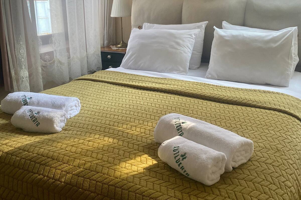 A hotel room with a bed, pillows, a nightstand with a lamp, and a painting on the wall.