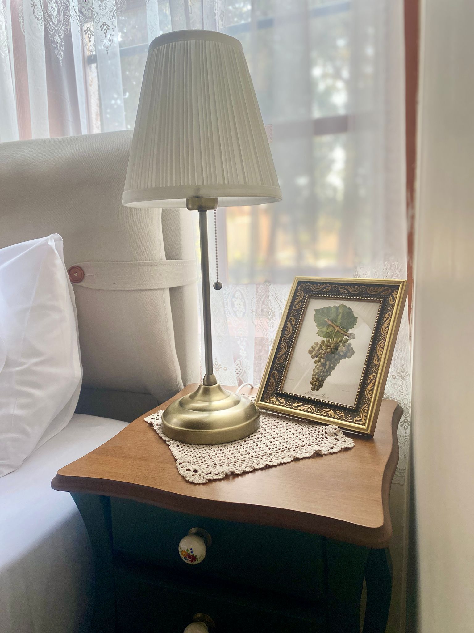 A bedside table with a lamp, a framed picture, and a pillow.