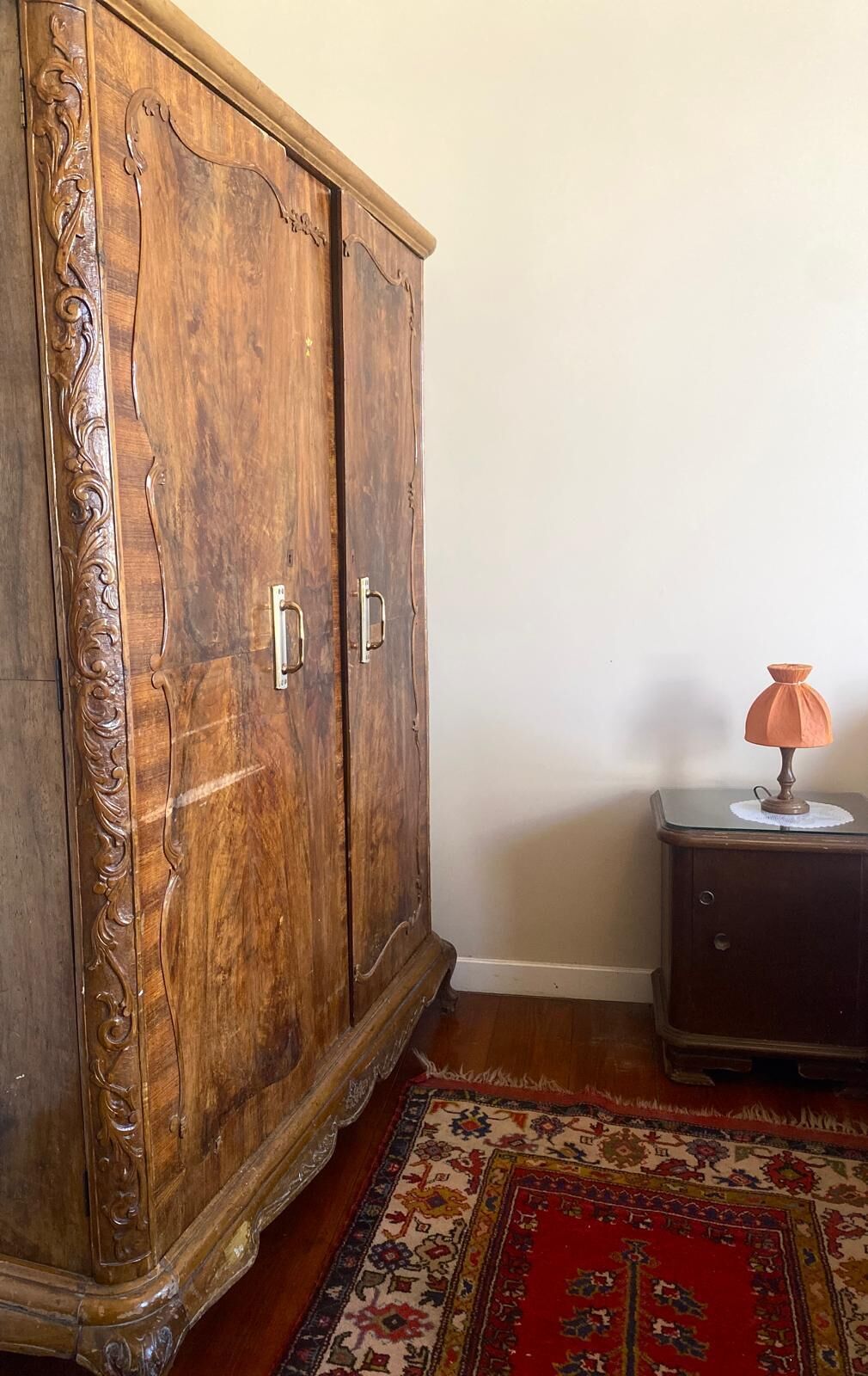 A wooden cabinet with ornate carvings, a small table with a lamp, and a patterned rug on a wooden floor.
