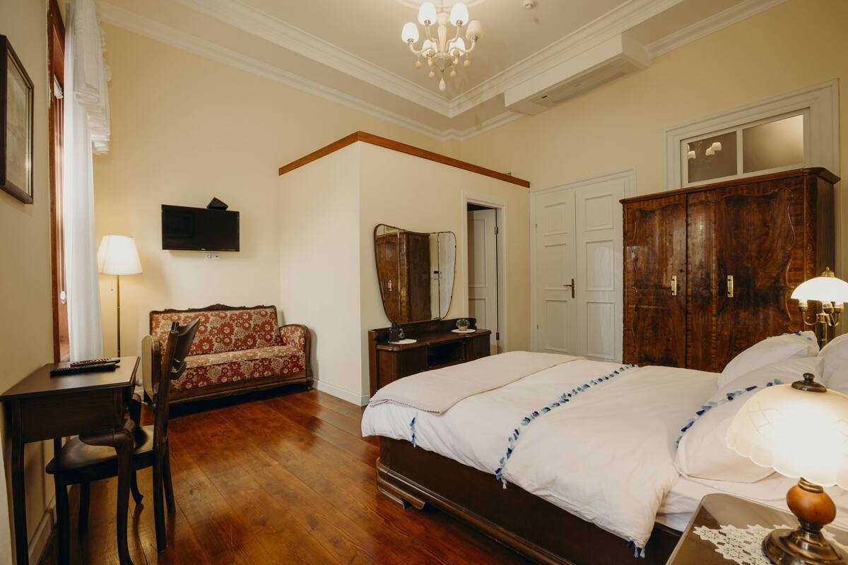 A bedroom with a large bed, wooden furniture, a television, and a chandelier.