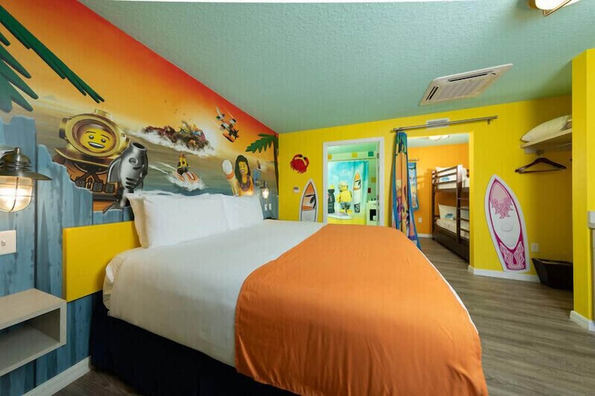 Une chambre d’hôtel avec un lit, une fresque murale, une armoire et une salle de bain visible à travers une porte ouverte.