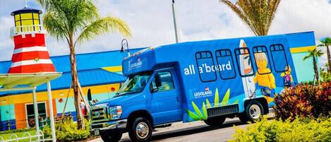A blue truck with 'Legoland' branding parked in front of a colorful building with a lighthouse.