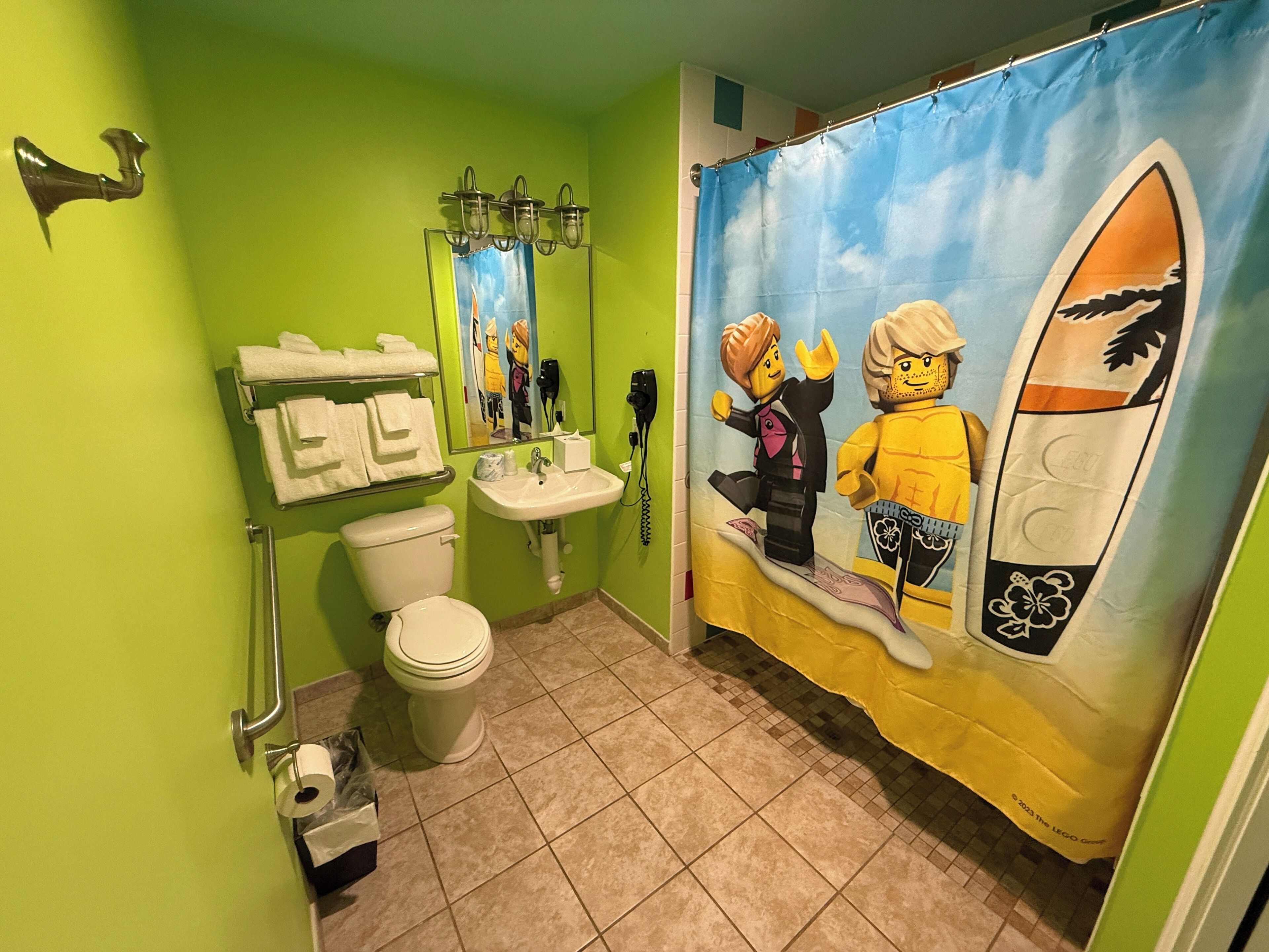 Un baño con inodoro, lavamanos y cortina de ducha con diseño de LEGO.