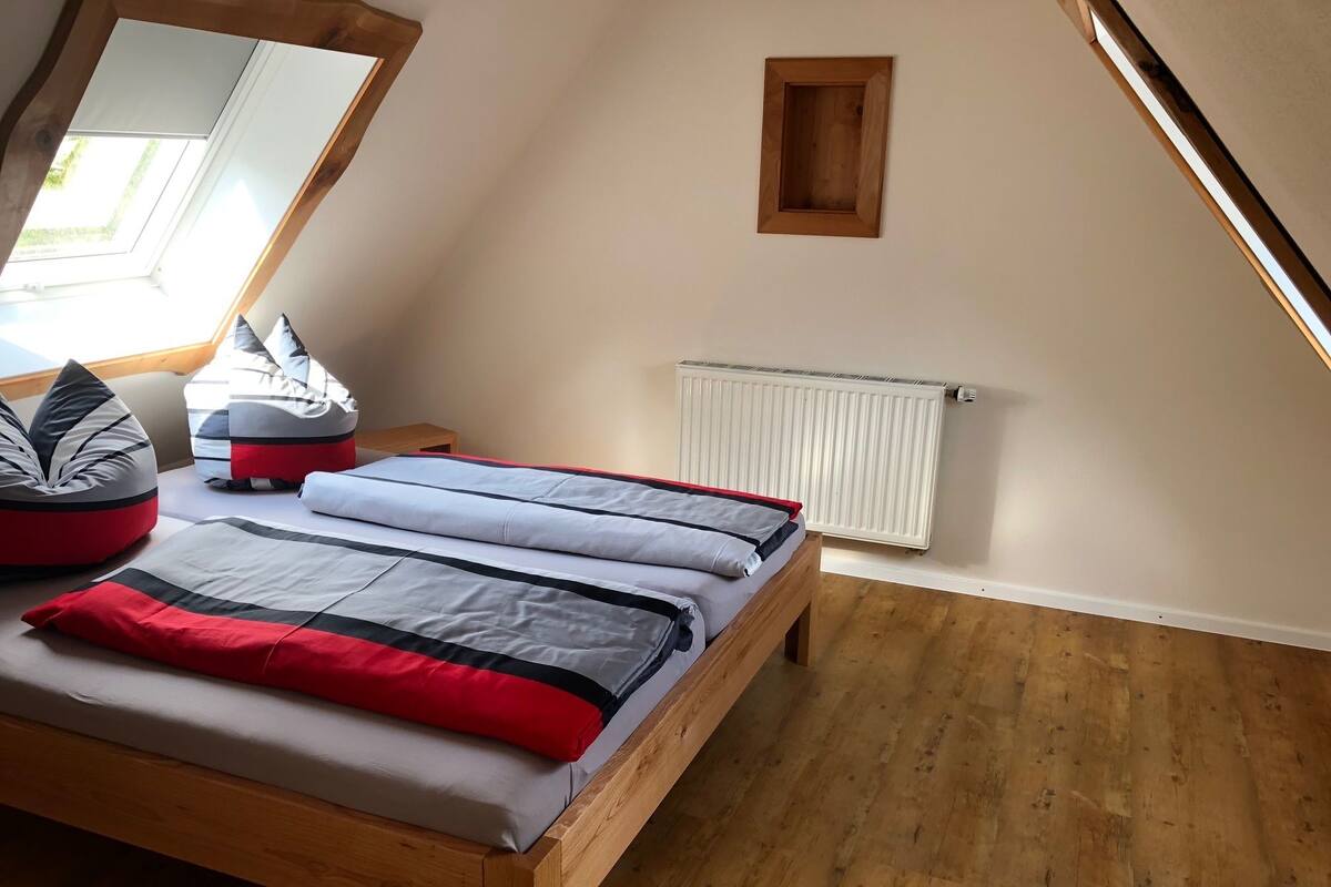 A bedroom with a sloped ceiling, a wooden bed, a radiator, and a small window.