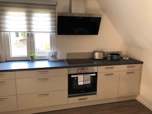 A modern kitchen with a built-in oven, a stovetop, and a flat-screen TV mounted above the counter.