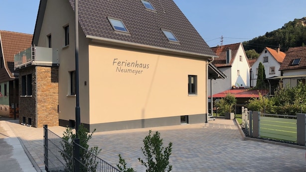 Ein modernes Gebäude mit einer beigefarbenen Fassade und einem geneigten Dach, mit der Aufschrift 'Ferienhaus Neumeyer'.