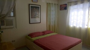 A bedroom with a bed, a window with curtains, a wall-mounted air conditioner, and a framed picture. - Anciano Beach House (Calatagan)