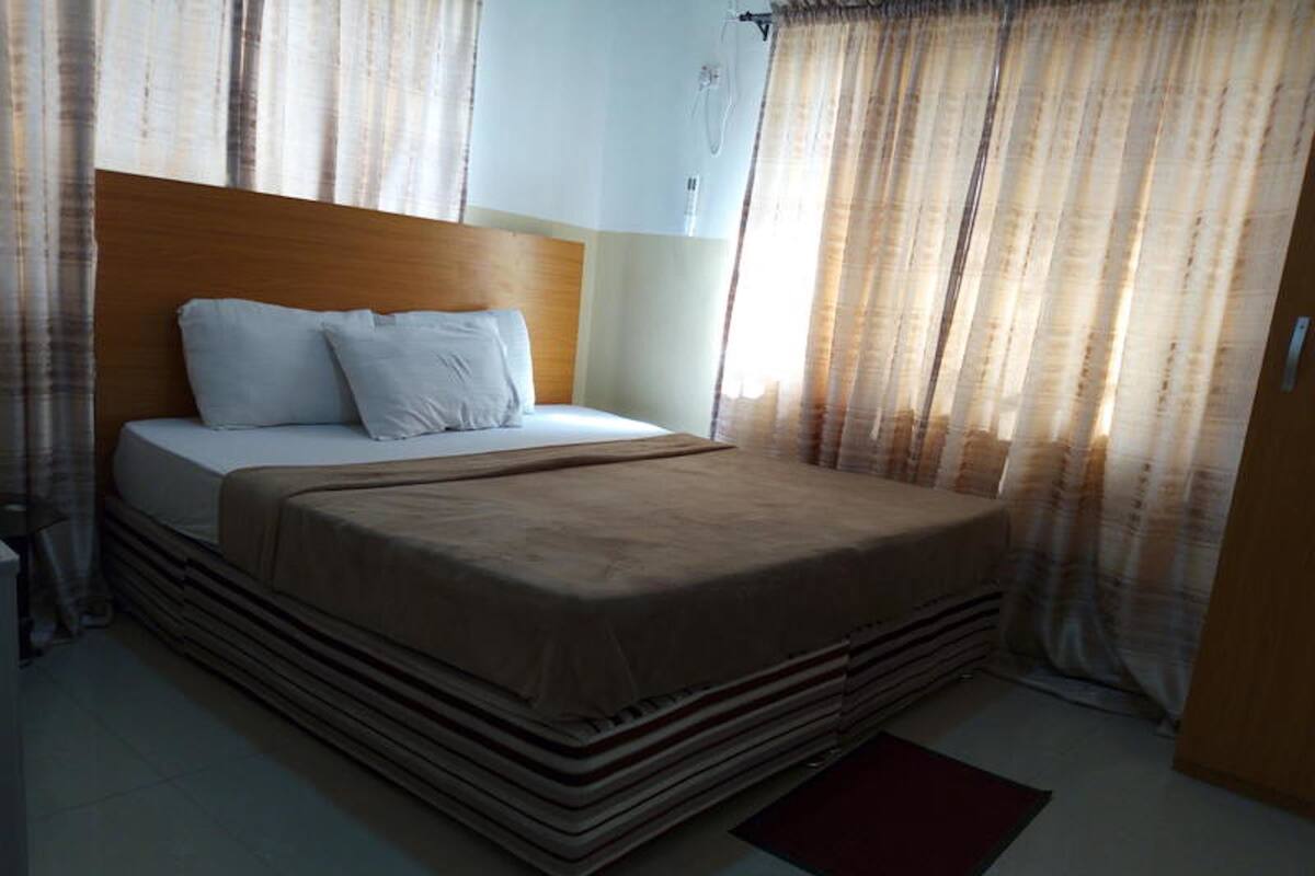A hotel room with a bed, curtains, a bedside table, and a red rug.