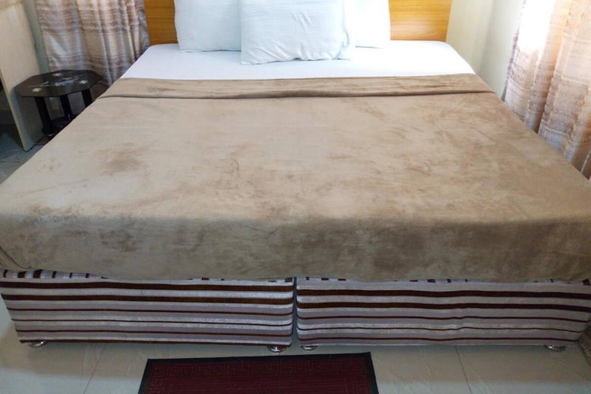 A bed with a beige cover, two white pillows, and striped bedding at the foot of the bed.
