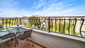 A balcony with a round table and two chairs, overlooking a residential area with buildings and greenery.