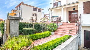 A residential building with a paved courtyard, a staircase leading to the entrance, and a well-maintained garden with various plants and shrubs.