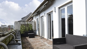 Une terrasse sur le toit, dotée d’un plancher en bois, de sièges extérieurs et offrant une vue sur le paysage urbain.